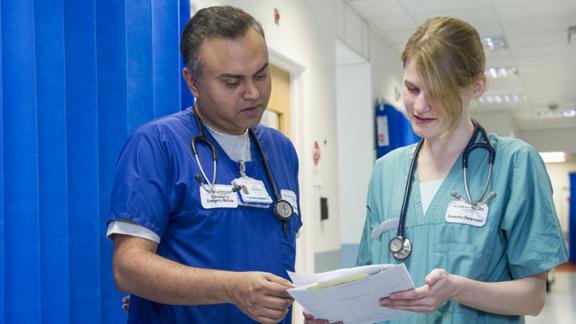 two NHS staff in scrubs discussing a document