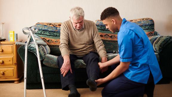 A care home worker checking a patient's leg mobility.