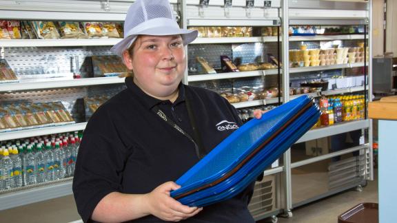 An apprentice caterer holding food trays.