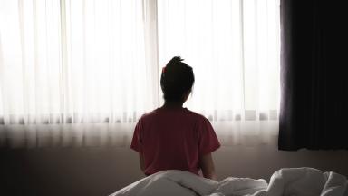 A silhouette of a person sitting on a bed by a window.