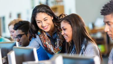 A diverse group of young people using a row of computers.