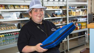 An apprentice caterer holding food trays.