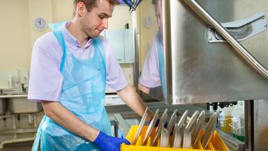 An apprentice dishwasher using an industrial dishwasher.