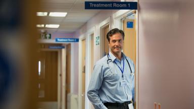 A doctor standing in the doorway of a hospital treatment room.