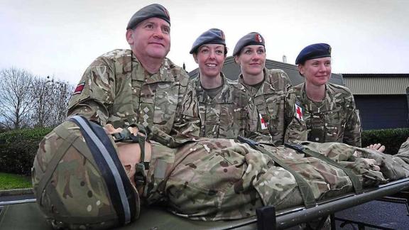 Four army reservists posing by a medical training dummy on a stretcher
