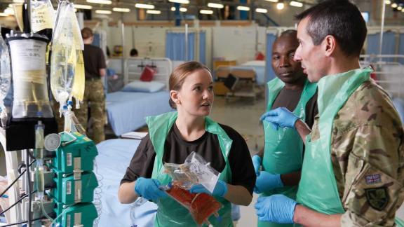 A diverse group of people talking with each other in medical PPE on a ward, representing the United Kingdoms Army Reservists.