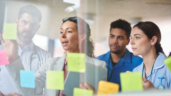 A diverse group of colleagues looking at memos on a glass wall.