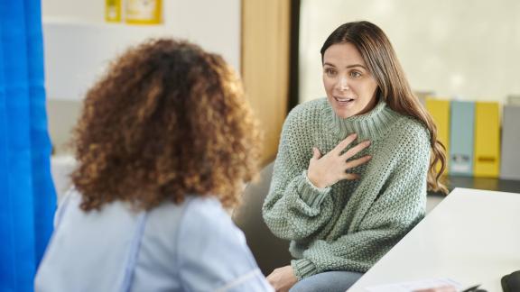 Person seated at a consultation desk speaking with a healthcare professional in a clinic.