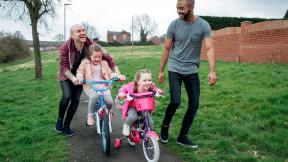 A couple with their daughters, riding bikes in the park