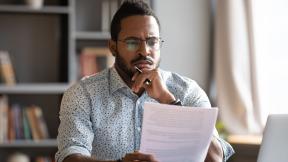 A home worker, deep in thought, reading a paper.