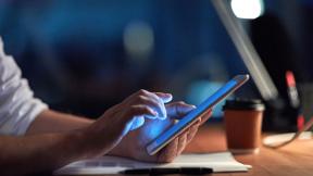 Someone using a tablet at a desk lit by a lamp.