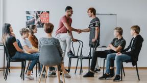 Two young people shaking hands in a diverse group counselling session.