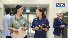 Two healthcare staff talking. The NHS logo in the top right of the image.