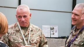 Three service personnel in uniform speaking with a civilian at a conference.