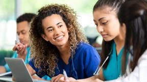 Healthcare professionals sit together at a table, collaborating and reviewing information on a laptop.