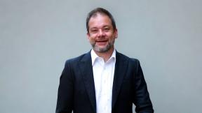 A head and shoulders picture of Ben Morrin who is wearing a blue suit jacket and white shirt against a plain grey background