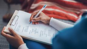 Close-up of a person holding a pen and completing a form on a clipboard.