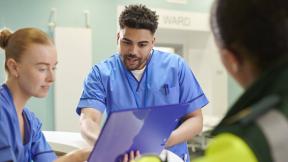 Healthcare workers reviewing paperwork together inside a hospital ward area.