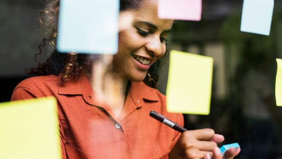 An office worker writing on a post-it note to be attached to a wall.