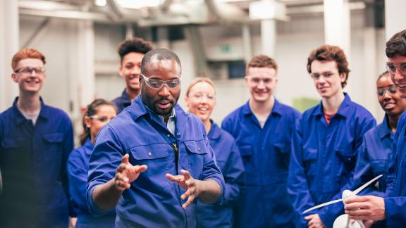 A diverse group of apprentices, wearing boiler suits, being taught