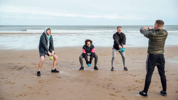 A diverse group of men exercising on a beach.