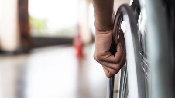 A close up of a hand pushing a wheelchair by the wheel handle.