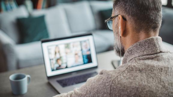 A homeworker from behind, with a video call on the screen.