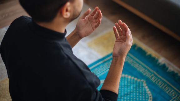 A man kneeling on a prayer rug and praying.