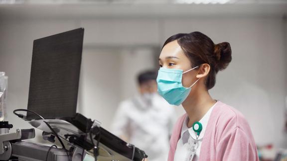 A masked healthcare worker checking a ward laptop.