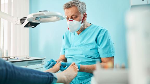 A masked podiatrist checking a patient's foot.