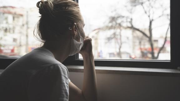 A masked woman looking out of a window.