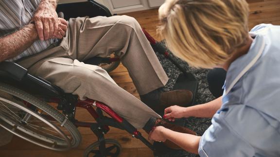 A nurse on a home visit, tying a patient's shoelace.