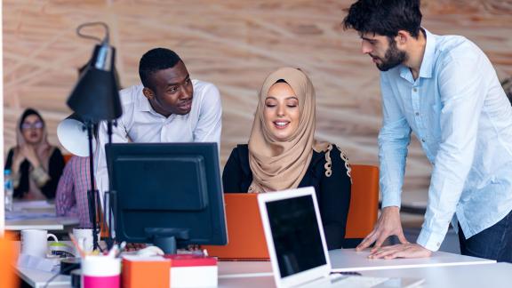 Three diverse office workers having a conversation at a desk.