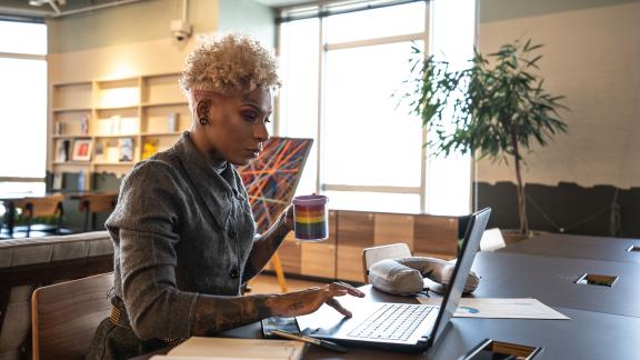 An office worker at their desk holding a pride mug.