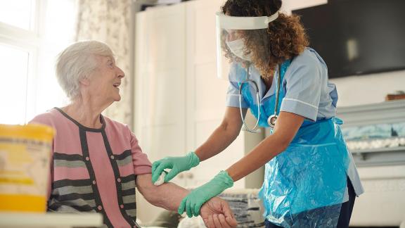 A nurse wearing full PPE, taking a patient's blood sample.