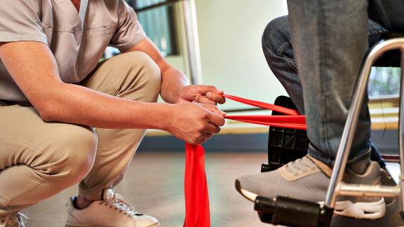 A physiotherapist stretching a band around a patient's leg.