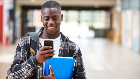 A student walking down a corridor and checking their phone.