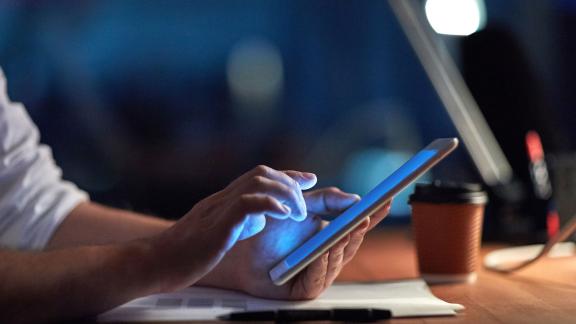 Someone using a tablet at a desk lit by a lamp.