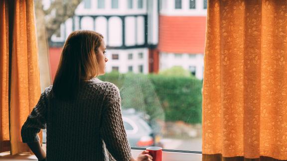 A woman holding a mug and looking out of a window.
