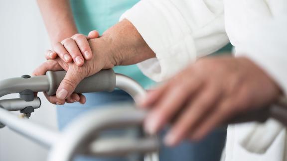A caring hand resting on the hand of someone using a Zimmer frame.
