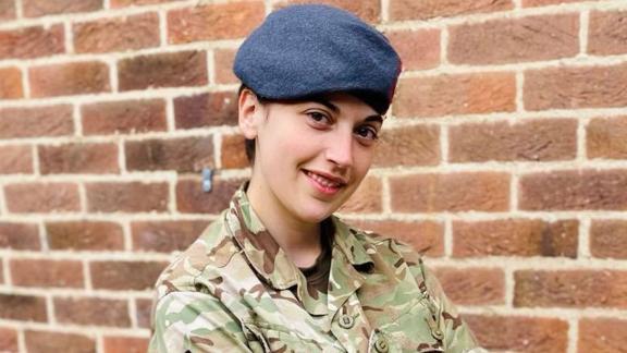 This image features a female Army Reservist in Uniform posting in front of a brick background.