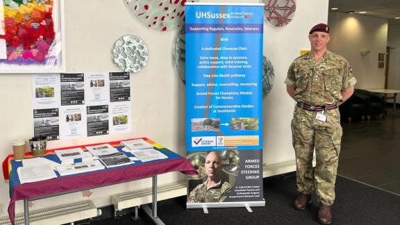 Army service personnel standing with a banner and stand at an Armed Forces event.