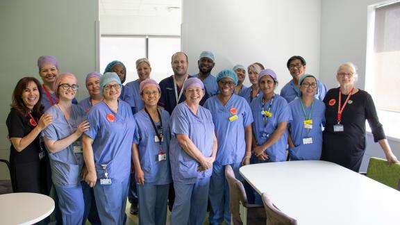 A large diverse group of NHS staff comprising of nurses, doctors and theatre staff with their managers. Posing for a phot in a breakroom.