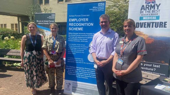 NHS staff and Armed Forces personnel standing with a banner outside a hospital.