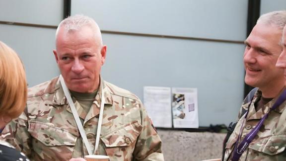 Three service personnel in uniform speaking with a civilian at a conference.