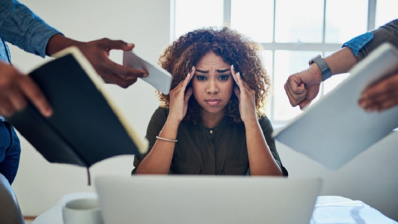 lady holding her head being stressed as many people are trying to get her attention 