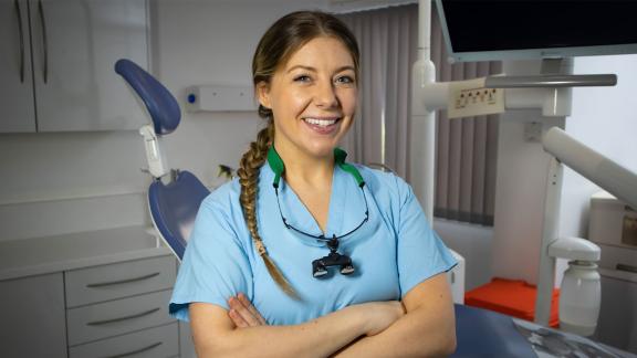Armed forces reservist in a dentists theatre wearing light blue scrubs with arms crossed.