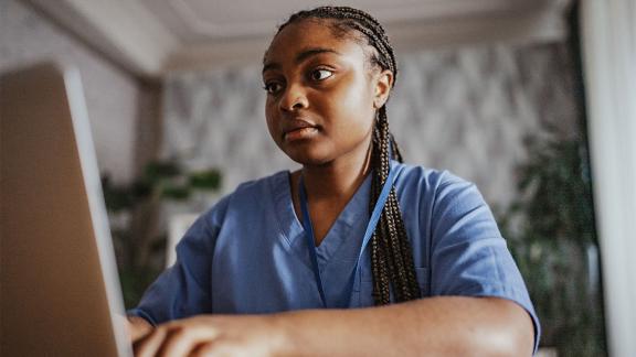 A healthcare worker in uniform works at a laptop in a quiet indoor setting.