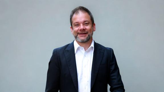 A head and shoulders picture of Ben Morrin who is wearing a blue suit jacket and white shirt against a plain grey background