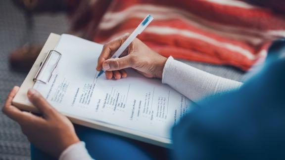 Close-up of a person holding a pen and completing a form on a clipboard.